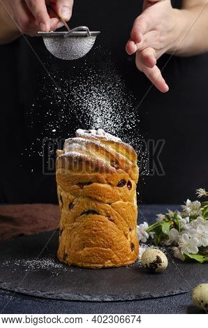 Female Hands Sprinkle With Powdered Sugar Craffin Cake On A Black Background. Traditional Seasonal B