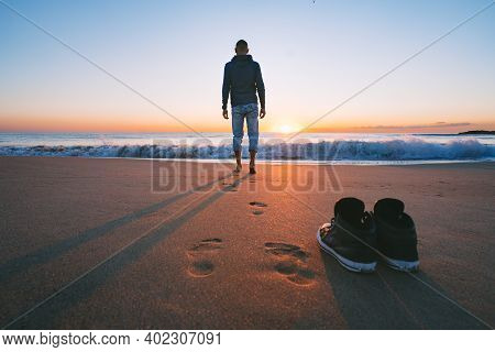 Carefree Barefoot Man Going To The Sea Or The Ocean Without Shoes On Sunset. Concept Of Freedom. Enj