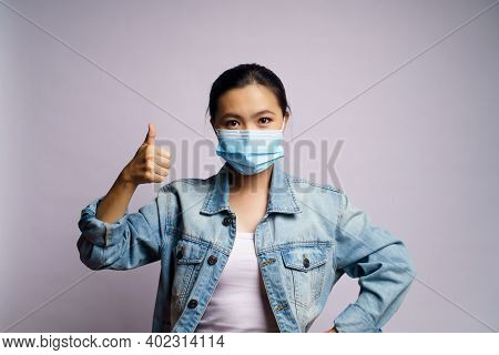 Asian Woman Wearing Protective Face Mask And Showing Thumb Up Isolated On White Background.