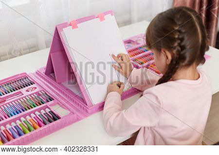Little Assiduous Female Kid Sitting At Table, Using Ruler For Drawing Tree, Painting With Set Of Art