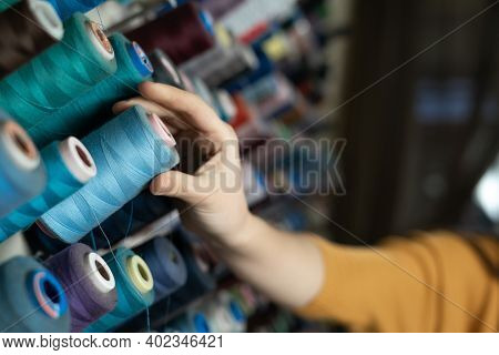 The Seamstresss Hand Takes A Skein Of Threads Of Different Colors From The Stand. A Tailor In A Sewi