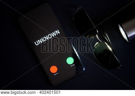 Smartphone With An Unknown Call, Sunglasses And A Flashlight Lie On A Black Surface. Problems Of Ano
