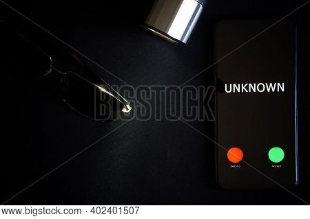 A Smartphone With An Unknown Call Lies On A Black Surface Next To Sunglasses And A Flashlight. The P