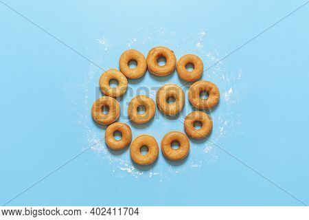 Yeast Raised Doughnuts Aligned In A Circle Shape, On A Blue Background. Flat Lay With Ring Donuts On