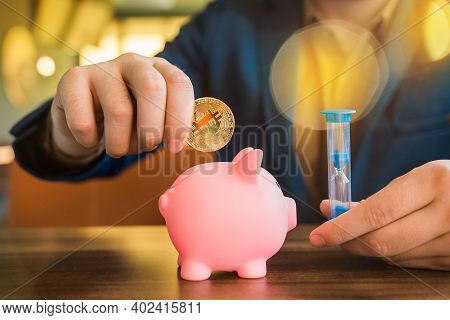 Businessman Hands Hold Gold Bitcoin Cryptocurrency And Hourglass Next To Pig Piggy Bank On The Table