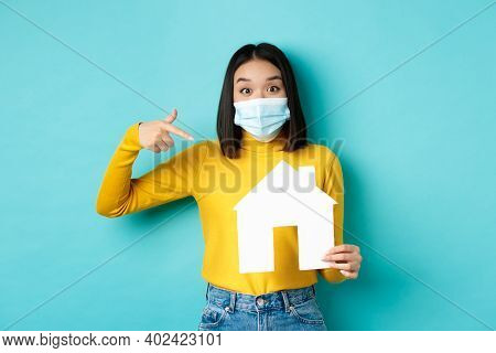 Covid-19, Pandemic And Real Estate Concept. Cheerful Asian Woman Smiling In Medical Mask, Showing Pa