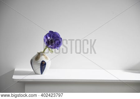 One Blue Anemone In A Multi-colored Vase In The Style Of The Seventies On The Table With Books As An