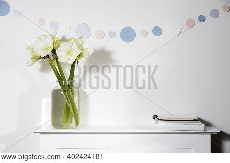 Bouquet Of White Amaryllis In A Tall Vase On The Fireplace. Round Garland From Paper