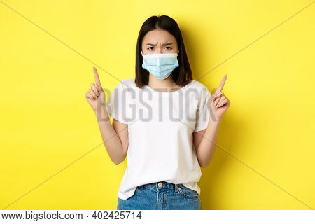 Covid-19, Pandemic And Social Distancing Concept. Disappointed Asian Girl In Medical Mask, Frowning 