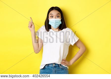 Covid, Health Care And Pandemic Concept. Asian Female Model In Medical Mask And White T-shirt Pointi