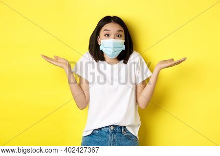 Covid-19, Quarantine And Social Distancing Concept. Clueless Asian Woman In Medical Mask Shrugging S