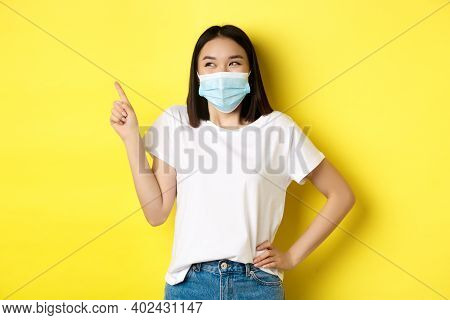 Covid, Health Care And Pandemic Concept. Asian Woman In Medical Mask And White T-shirt Pointing Fing