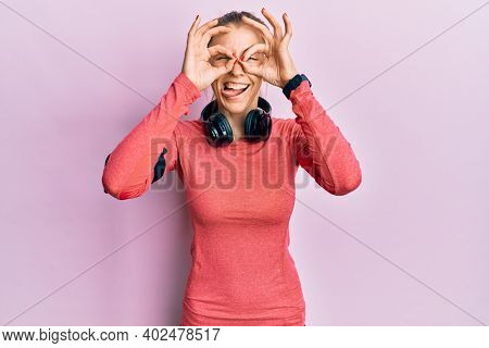 Beautiful caucasian woman wearing sportswear and arm band doing ok gesture like binoculars sticking tongue out, eyes looking through fingers. crazy expression. 