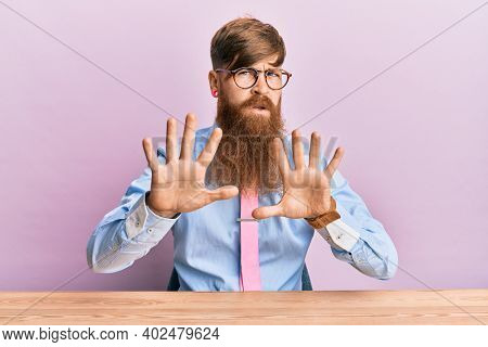 Young irish redhead man wearing business shirt and tie sitting on the table moving away hands palms showing refusal and denial with afraid and disgusting expression. stop and forbidden. 