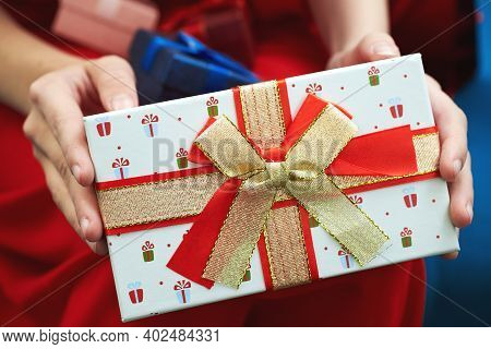 Female Hands Holding Gift Box With A Red And Gold Bow.