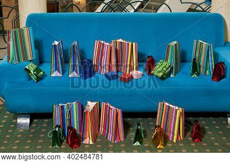 A Lot Of Multicolored Paper Gift Shopping Bags On The Turquoise Sofa At The Mall.