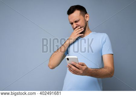 Photo Of Dissatisfied Shocked Handsome Young Man With Beard Wearing Everyday Blue T-shirt Isolated O