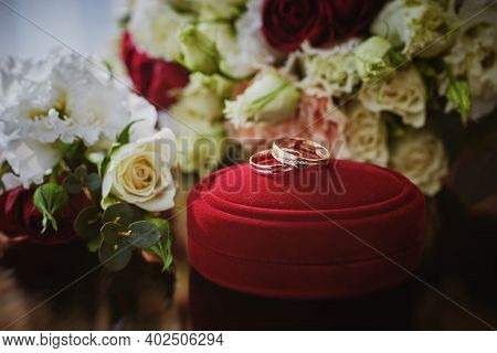 Close Up View Of Wedding Rings On A Red Velvet Box And Flowers On A Glass Table In The Hotel Room.