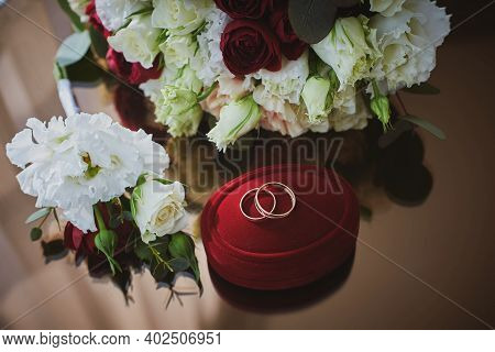 Close Up View Of Wedding Rings On A Red Velvet Box And Flowers On A Glass Table In The Hotel Room.