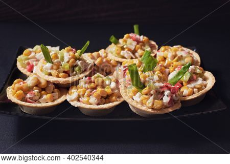 Canapes In Tartlets, Tasty Snack. Tartlets With Crab Sticks And Canned Corn Salad On A Black Rectang