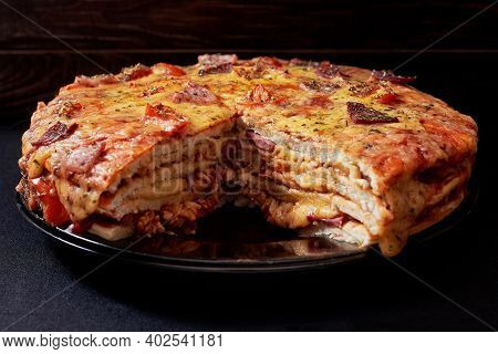 Italian Pizza Cake With Four Layers Full Of Grilled Salami, Ham And Moose Sausage. Black Background.