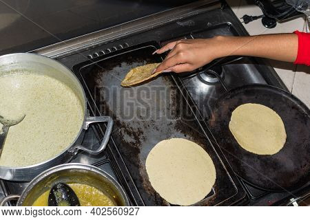 Hand Of A Young Woman Taking Out A Tortilla From The Comal In Her Kitchen House