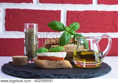 Rapeseed Oil, Basil, White Bread Croutons With Mozzarella, Spices And Tomato On A Stone Stand On A B