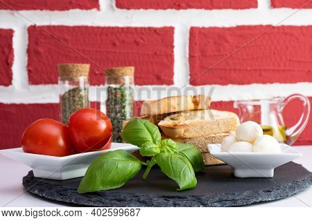 Rapeseed Oil In A Jug, Basil, White Bread Croutons With Mozzarella, Spices And Tomatoes In A Saucer 