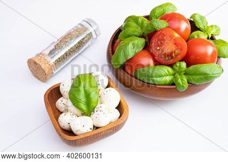 Fresh Tomatoes And Green Basil In A Wooden Bowl, Near Spices And Mozzarella In A Wooden Bowl On A Wh