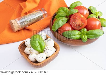 Fresh Tomatoes And Green Basil In A Wooden Bowl, Next To Mozzarella In A Wooden Bowl And Spices On A