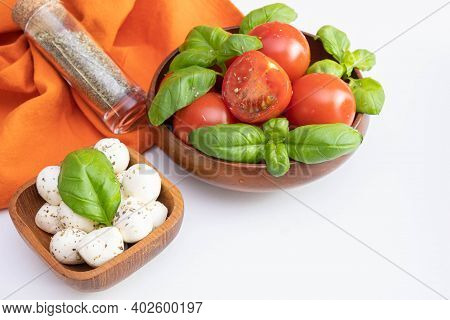 Fresh Tomatoes And Green Basil In A Wooden Bowl, Next To A Small Mozzarella In A Wooden Bowl And Spi