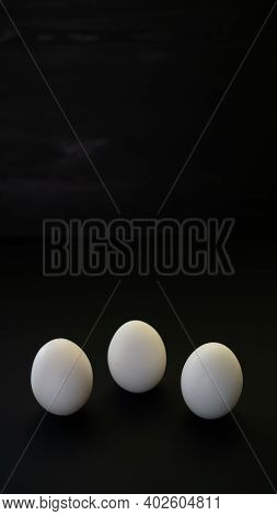 Composition Of Three Chicken Eggs With White Shell Of Boiled Or Raw. White And Black Contrast In Egg
