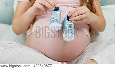 Closeup Of Pregnant Woman Waiting For Baby Boy Holding Small Baby Boots In Hands. Concept Of Pregnan