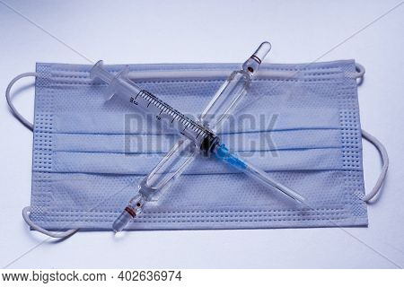The Syringe And Ampoules Lie On A Medical Mask In The Form Of A Cross.