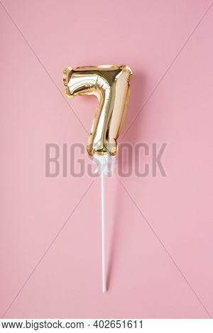 Gold Inflatable Number 7 On A Stick On A Pink Background.