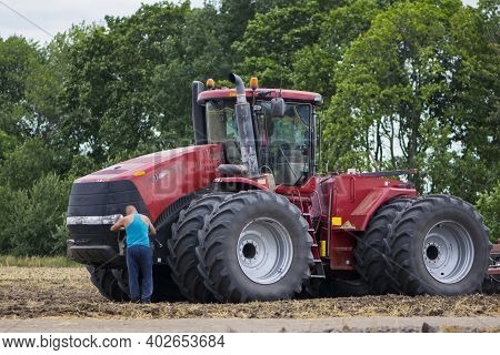 Tractor Driver Near A Large Red Tractor. A Farmer On A Tractor Prepares Land For A Seeding Tractor W