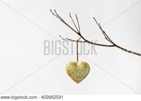 Gold Patterned Metal Heart On A String Hanging On A Bare Winter Tree Branch Against A White Backgrou