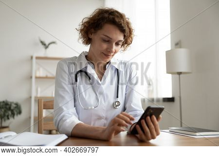 Smiling Pleasant Young Female General Practitioner Using Mobile Phone.
