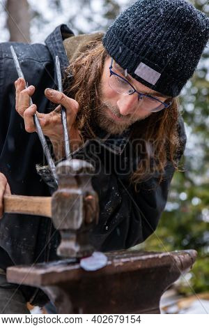Close Up Shot Of A Young Blacksmith Under The Snow, Concentrated In Hammering And Flattening A Red, 