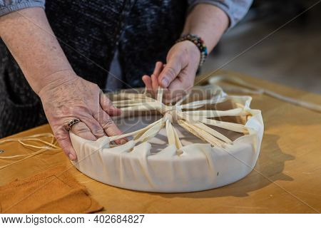Close Up Of Womans Hands Pulling The Ends Of A Piece Of Leather Around A Wooden Support To Create A 