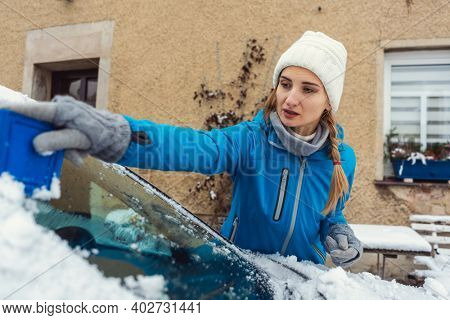 Woman scraping off ice from front window of her car in winter being a bit annoyed