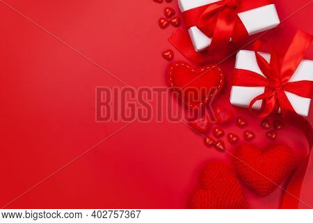 Valentines day greeting card template. Gift boxes, heart decor and candy sweets over red background. Top view flat lay with copy space