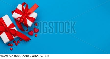 Valentines day greeting card template. Gift boxes and heart candy sweets over blue background. Top view flat lay with copy space