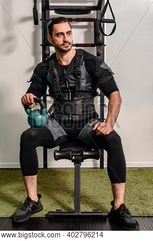 Portrait Of Young Concentrated Athletic Man In Ems Suit Holding Dumbbell