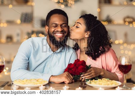 Celebrating Special Day. Beautiful Black Girlfriend Kissing Her Smiling Boyfriend In Cheek, Holding 