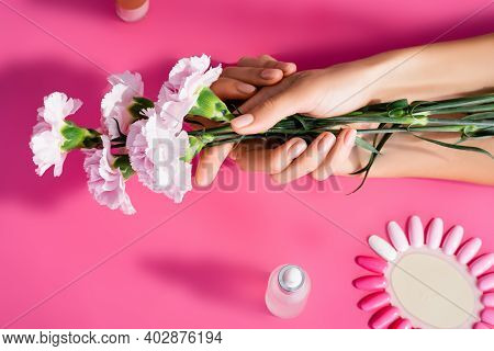 Cropped View Of Woman Holding Carnation Flowers Near Palette Of Artificial Nails And Cuticle Remover