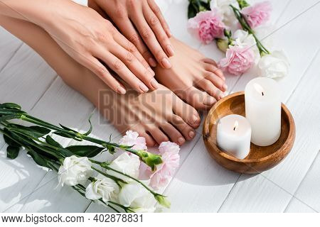 Female Feet And Hands With Glossy Pink Nails Near Carnation And Eustoma Flowers And Candles On White