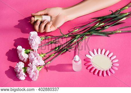 Cropped View Of Woman Holding Pastel Nail Polish Near Carnation Flowers, Cuticle Remover And Palette