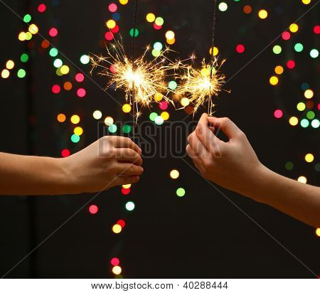 sparklers สวยงามในผู้หญิงมือบนพื้นหลังพวงมาลัย