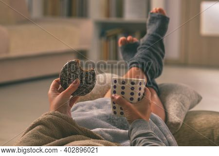 Woman with sweet gingerbread cookie and feet lying on pilow in the cozy room